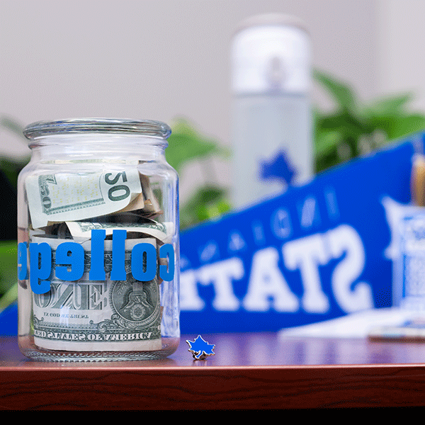 A photo of a jar that has cash in it and says “college” on the front of it. Indiana state gear is blurred in the background. 