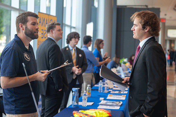 A photo of two men talking to one another at a job fair.