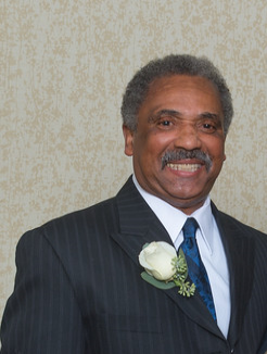 Portrait of Charlie Brown, an elder African American man smiling, wearing a dark suit with a white rose boutonniere.